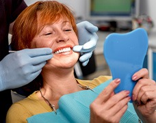 An older woman admiring her dentures while looking in a hand mirror