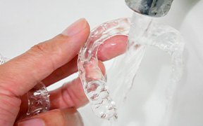 Closeup of fingers holding Invisalign under running water