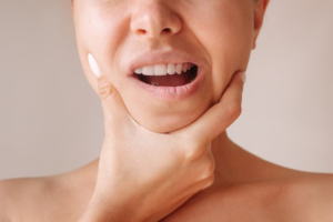 Close up of woman rubbing her jaw on taupe background