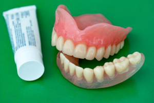 Dentures next to denture adhesive on a green background